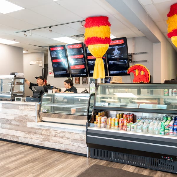 Two Generations Kitchen employees behind a counter with menu boards, food displays, and drink refrigerators.